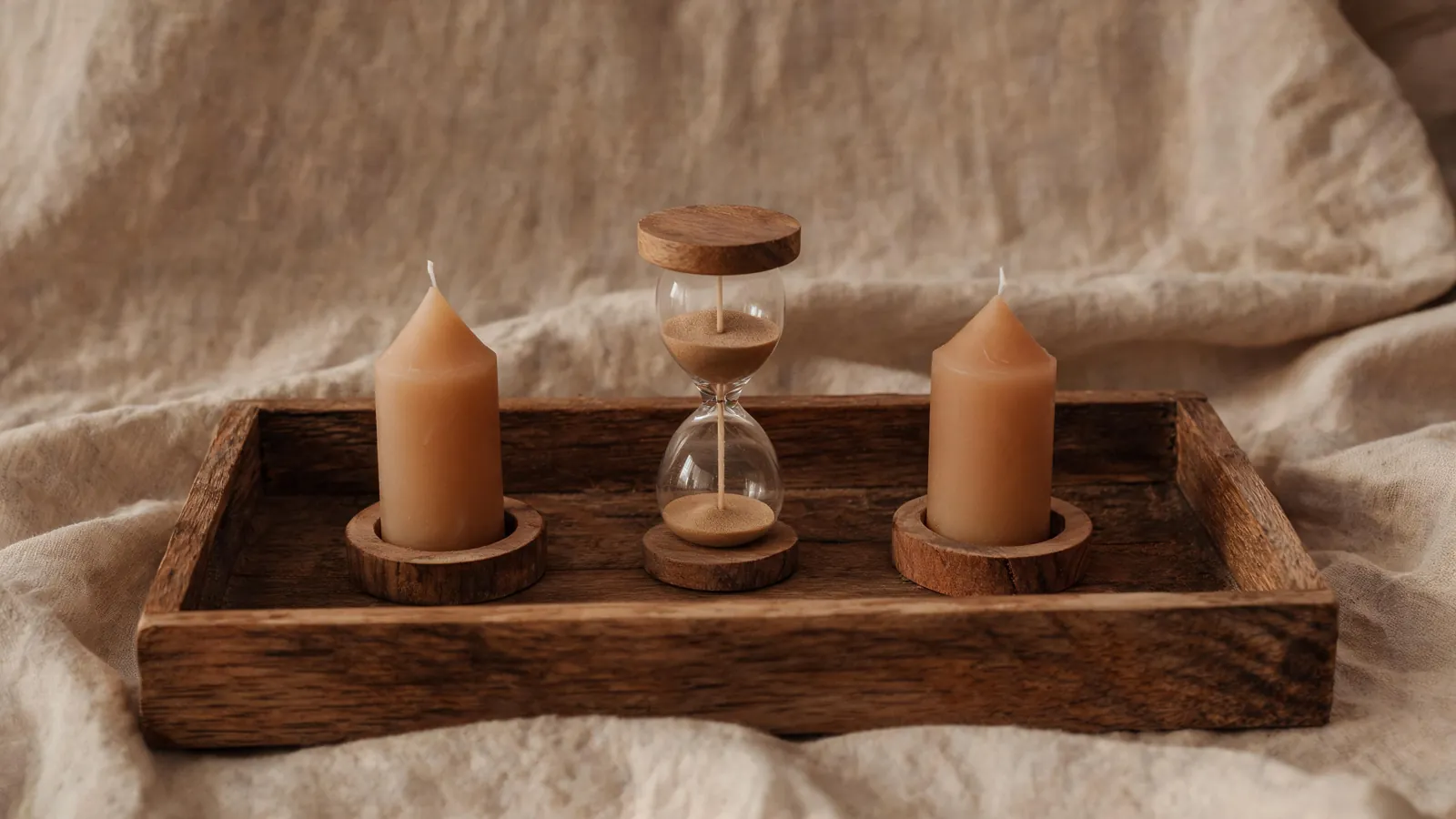 An hourglass between two candles on a wooden tray