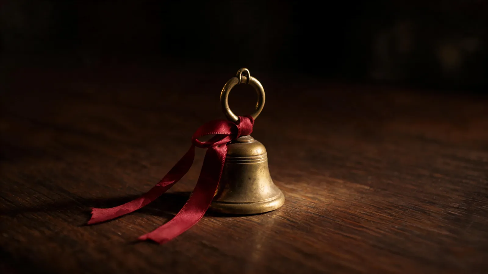A small brass bell and a red ribbon on dark wood
